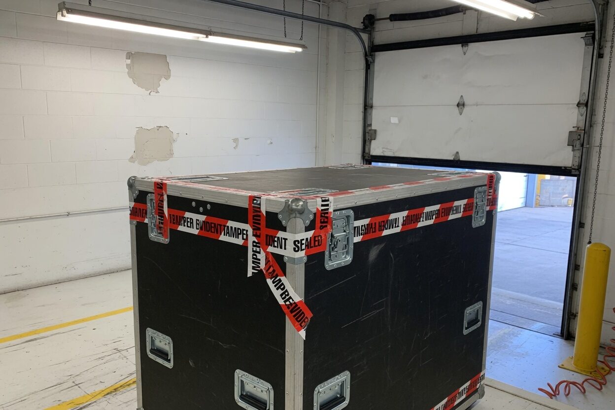 Sealed black equipment crate with tamper tape in a white loading bay.