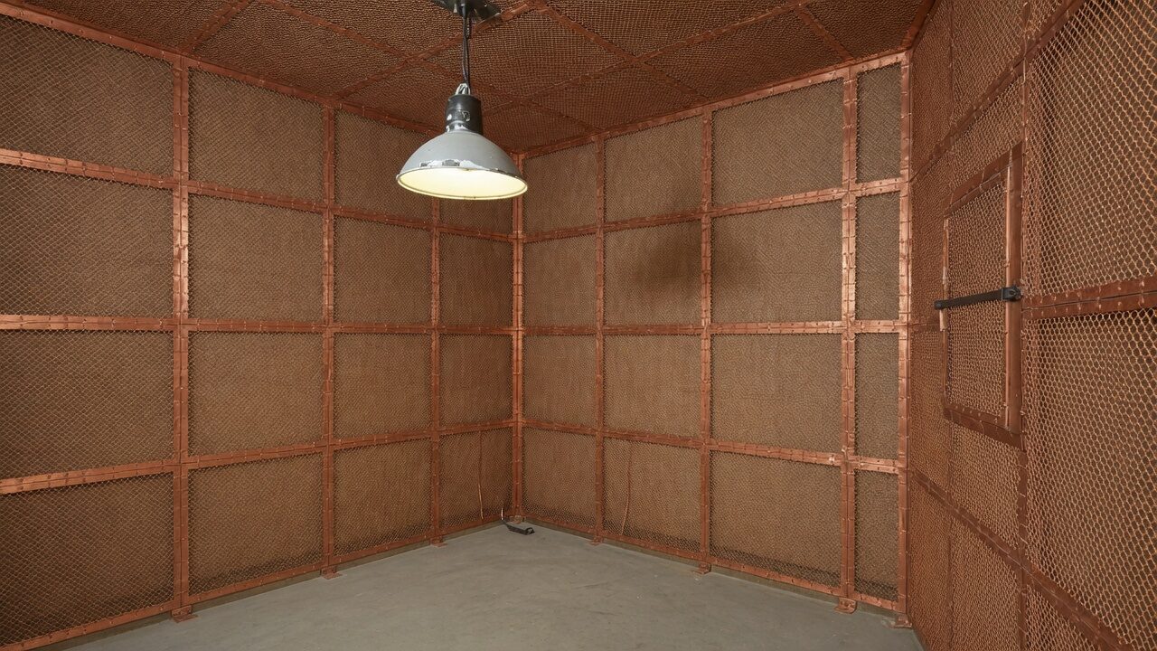 Empty Faraday cage room, copper mesh walls and ceiling, a single industrial lamp.
